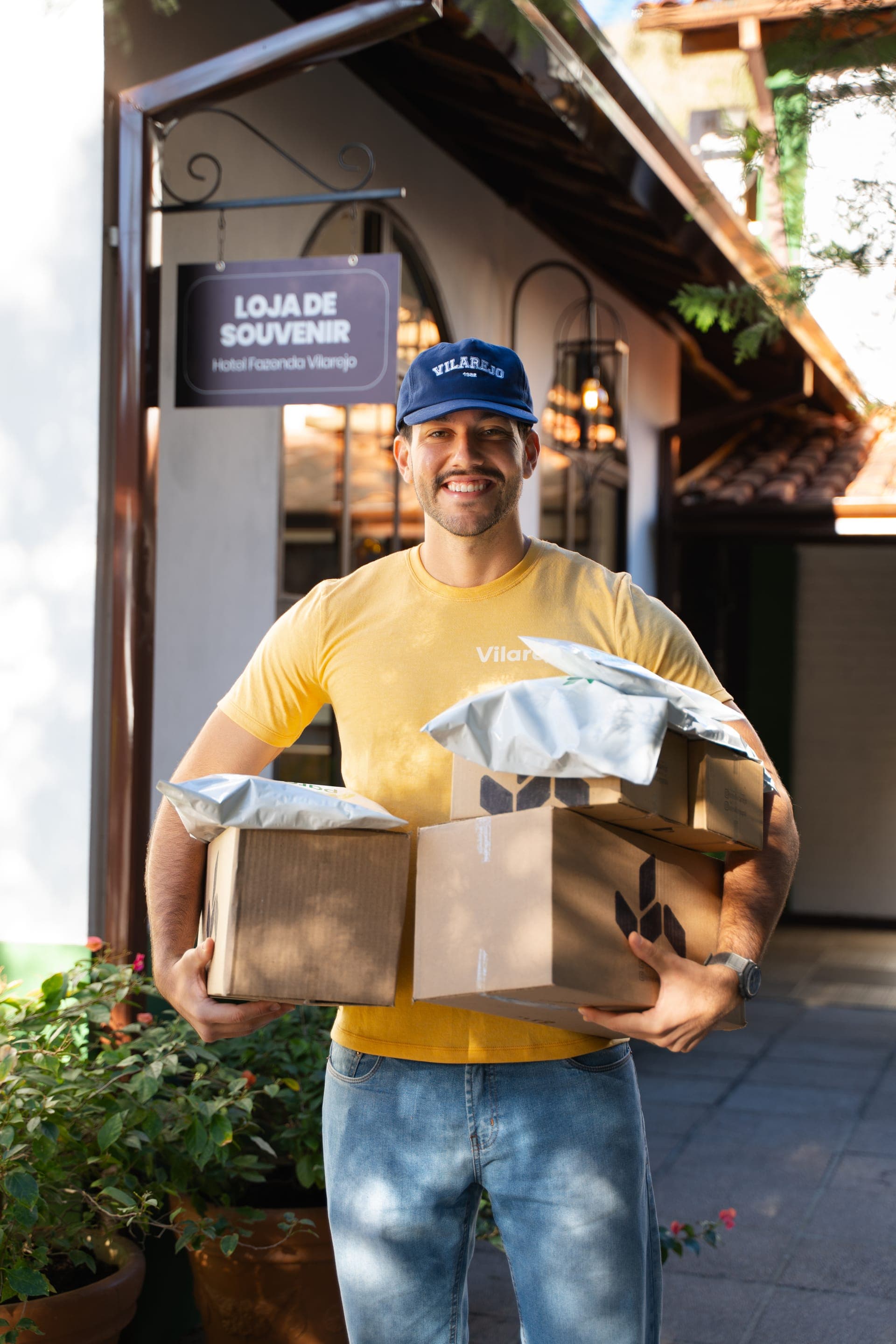 Rapaz com camiseta e boné Vilarejo segurando caixas de produtos embalados para envio